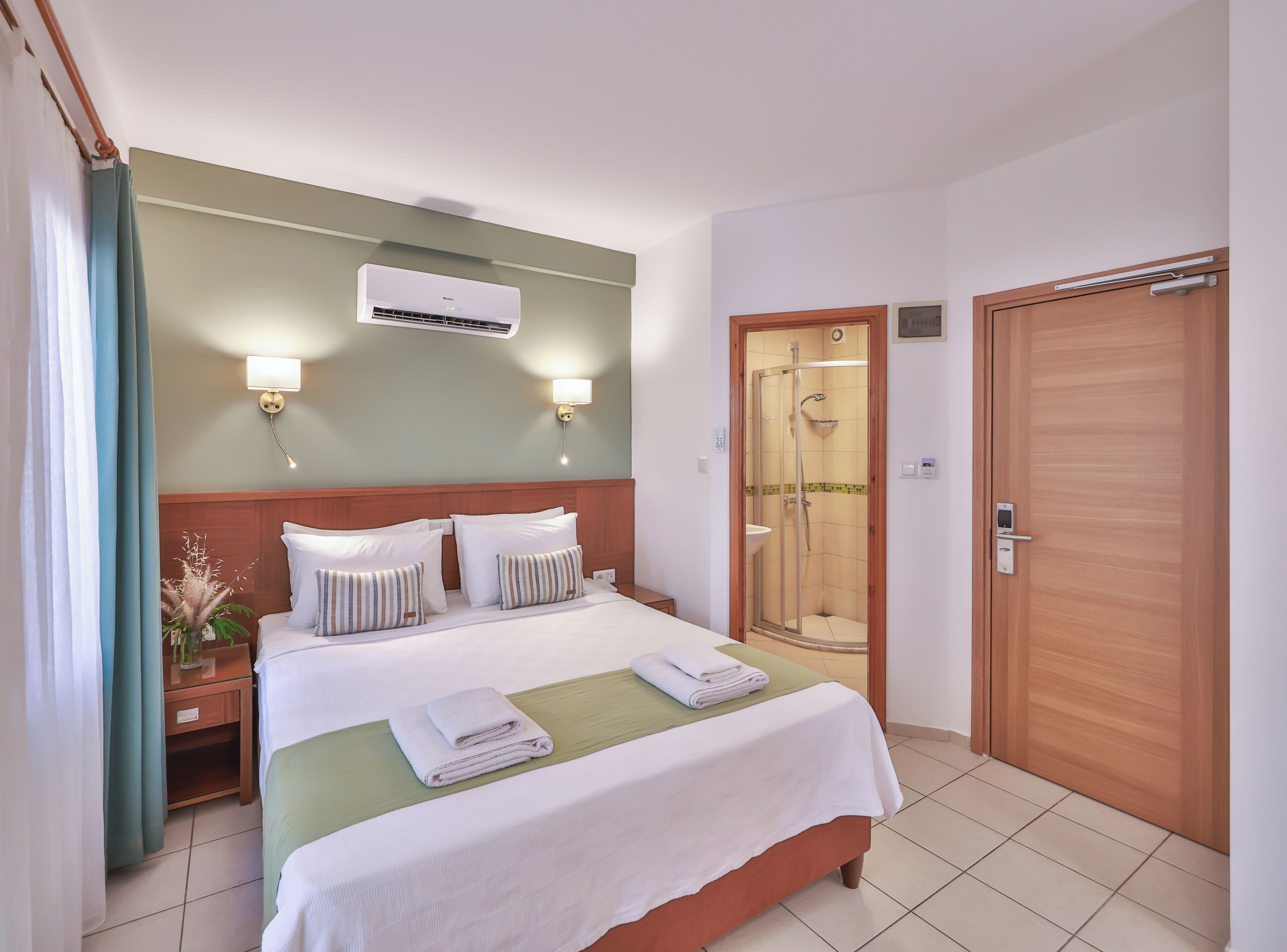 Une chambre d’hôtel équipée d’un lit, d’une douche, d’un climatiseur et d’une porte en bois.