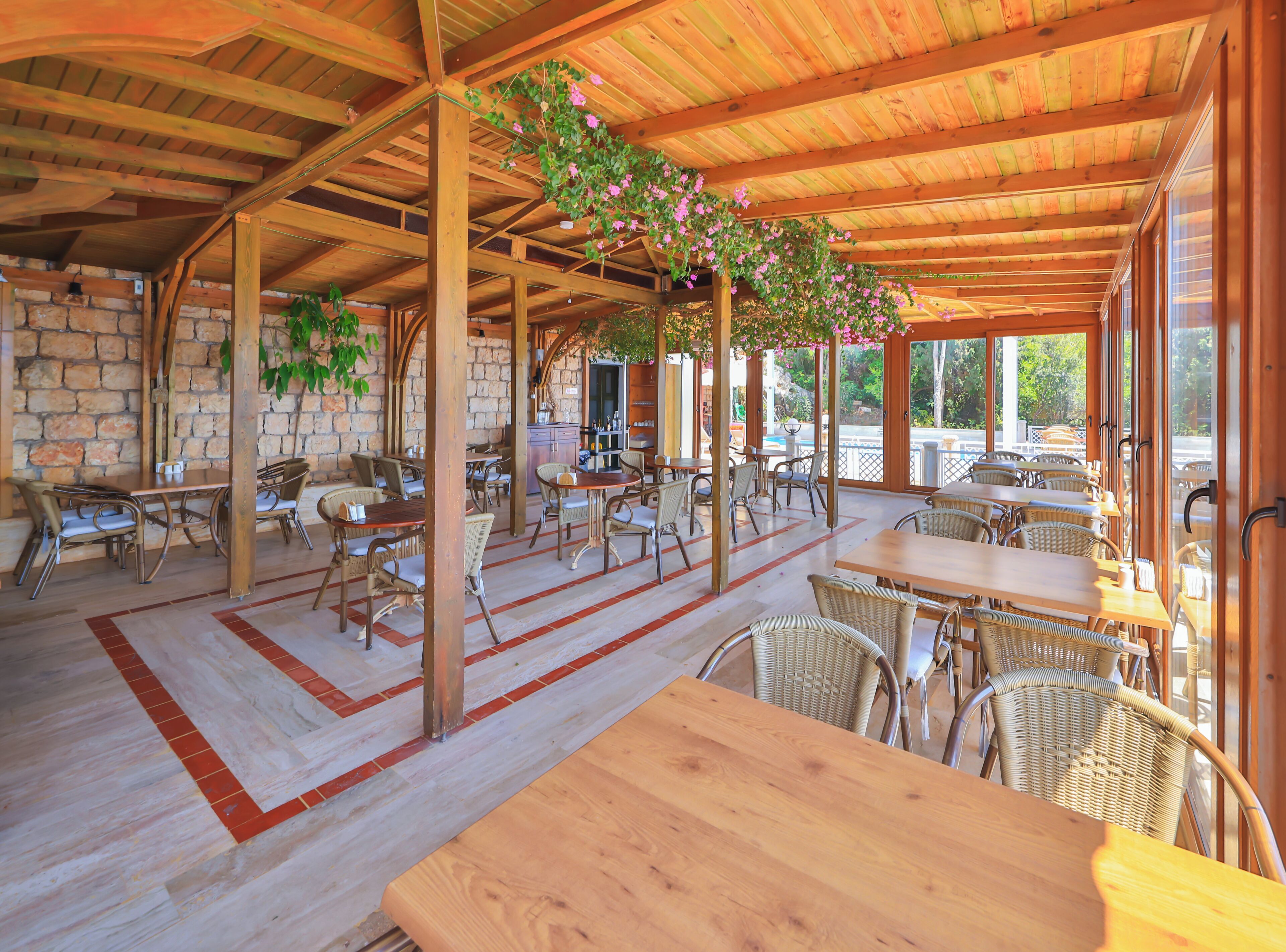 Een terras met houten tafels en stoelen, stenen muren en uitzicht op de straat.