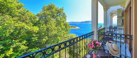 A balcony with a view of the sea, a table with a vase of flowers, and a chair.