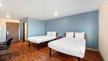 A hotel room with two single beds, a wooden floor, a desk with a chair, and a door leading to another room.