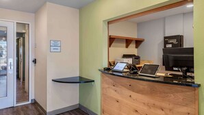 Un área de recepción con mostrador de registro de entrada y salida, una computadora portátil, una impresora y un cartel que indica espacio de oficinas.