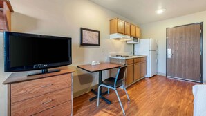 Cocina compacta con armarios de madera, microondas, refrigerador, una mesa de comedor con una silla y un televisor de pantalla plana.
