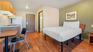 Un dormitorio con cama, escritorio con silla, kitchenette y una puerta que da a otra habitación.