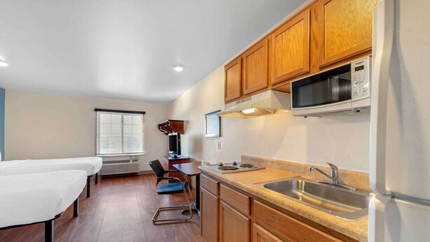 Una cocina compacta con armarios de madera, un microondas, una estufa y un lavabo. Hay un pequeño comedor con una mesa y sillas.