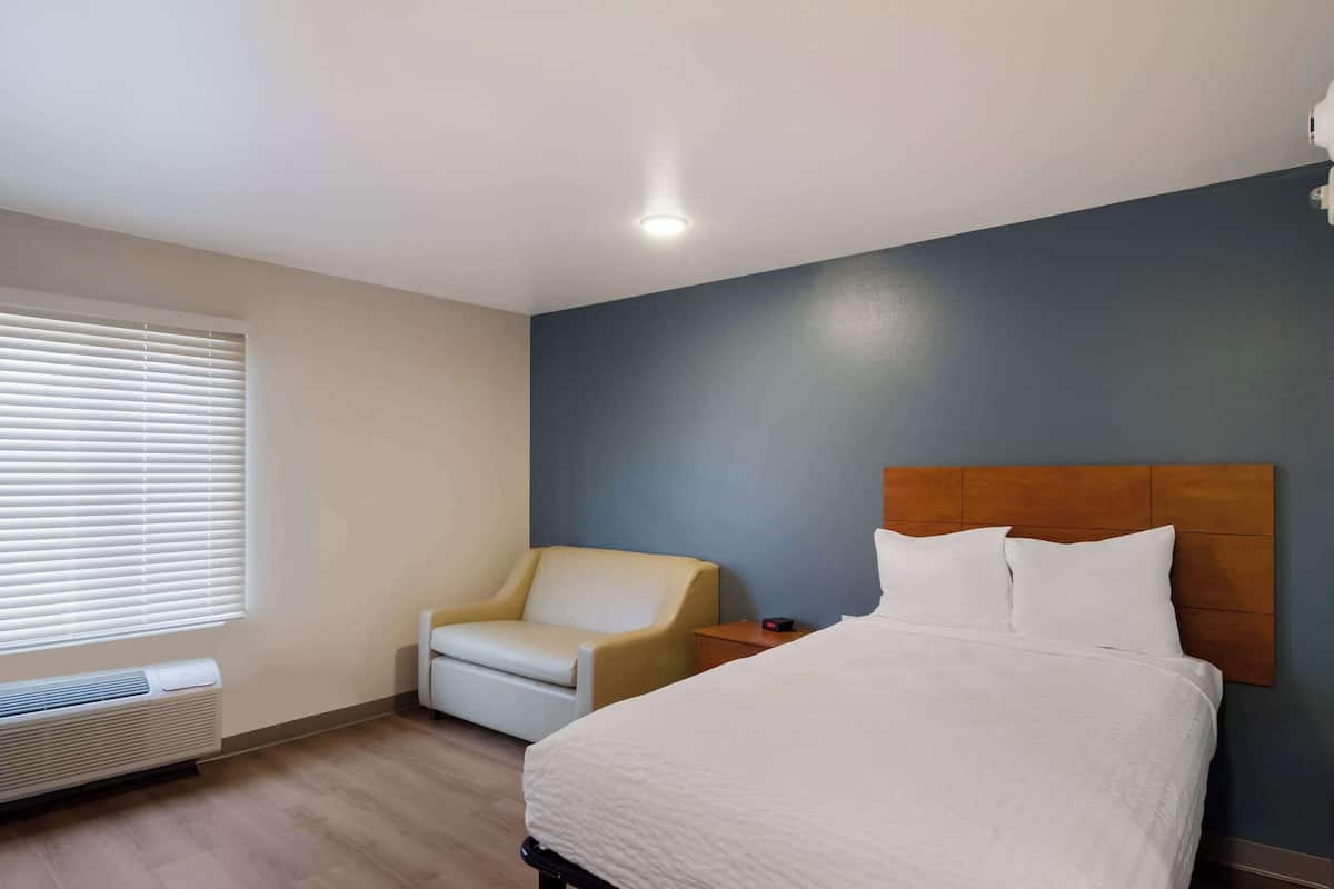 Una habitación de hotel con cama, una silla, una mesita de noche y una ventana con persianas.