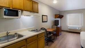 A compact kitchen with wooden cabinets, a microwave, a sink, and a dining area with a table and chairs. - WoodSpring Suites Jacksonville East 295 Cruise Port (Jacksonville)