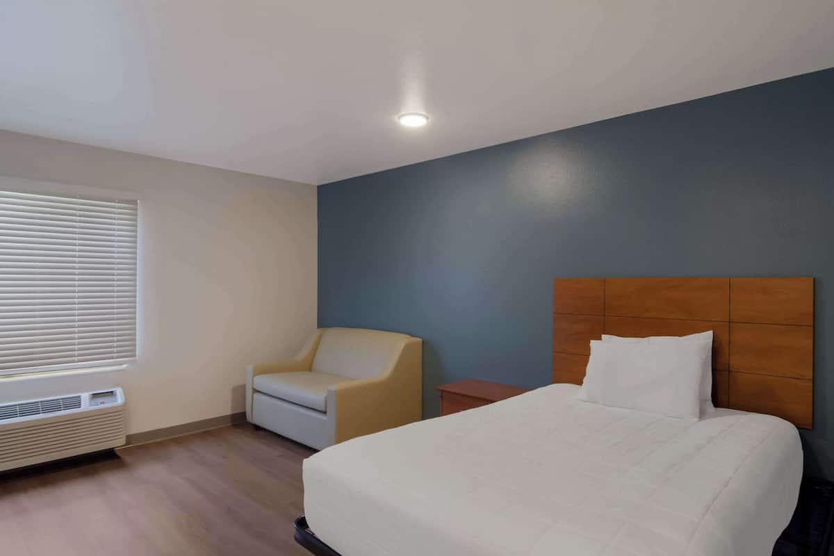Una habitación de hotel con cama, una silla, una mesita de noche y una ventana con persianas.
