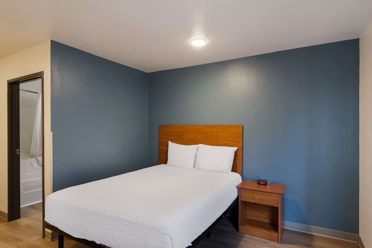Una cama bien tendida con ropa blanca en una habitación con paredes azules y un cabecero de madera.