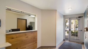 A hotel lobby with a wooden panel wall, a reception desk, a large mirror, and a door leading outside. - WoodSpring Suites Jacksonville East 295 Cruise Port (Jacksonville)