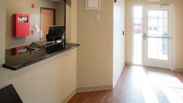 A hotel lobby with a reception desk, a fire alarm, an exit sign, and a door leading outside.