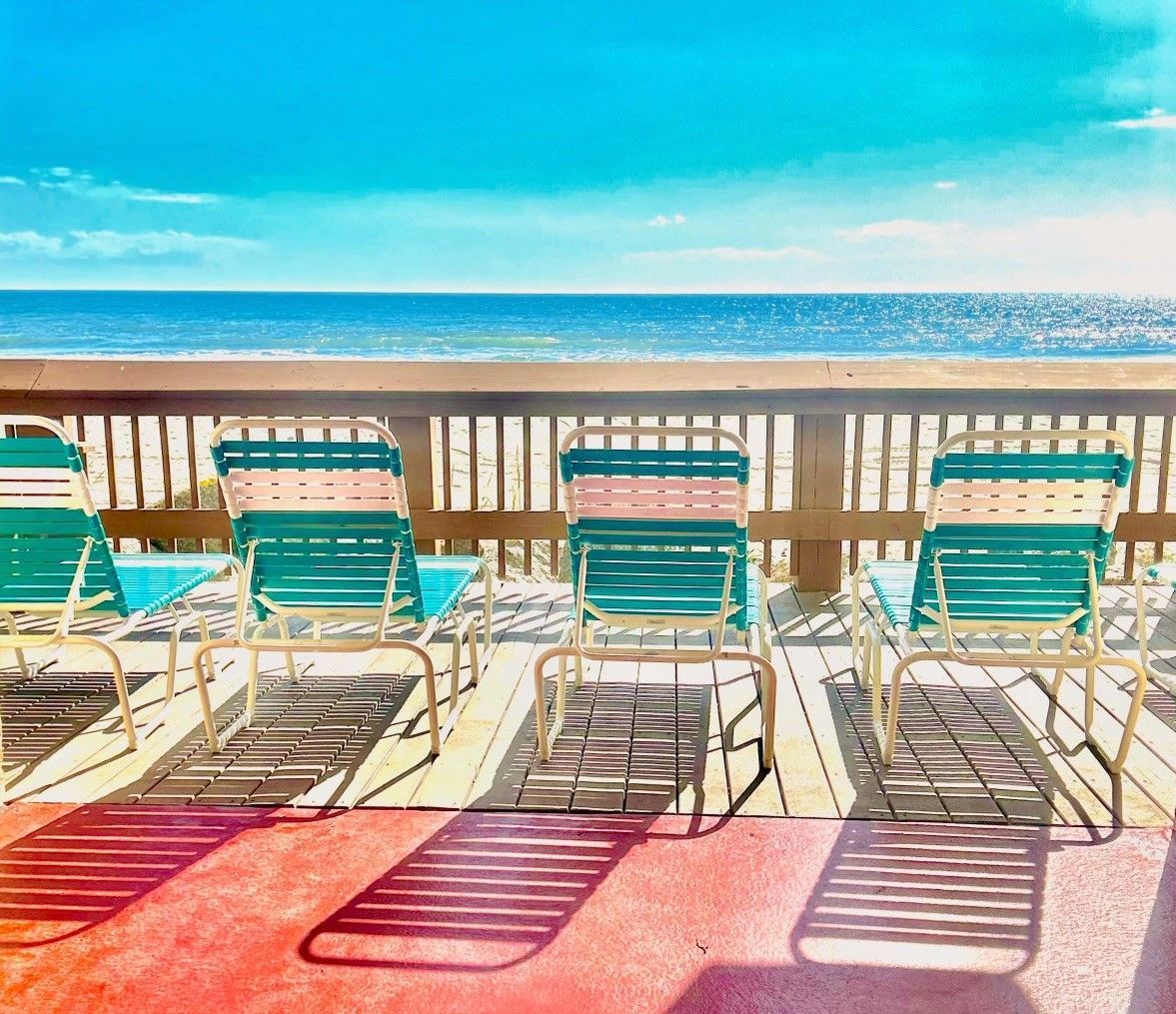 A beachside deck with metal chairs and a wooden railing, overlooking the ocean.