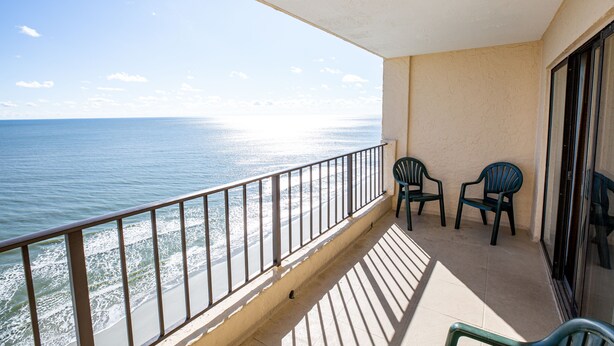 A balcony with a view of the ocean, two chairs, and a glass door.