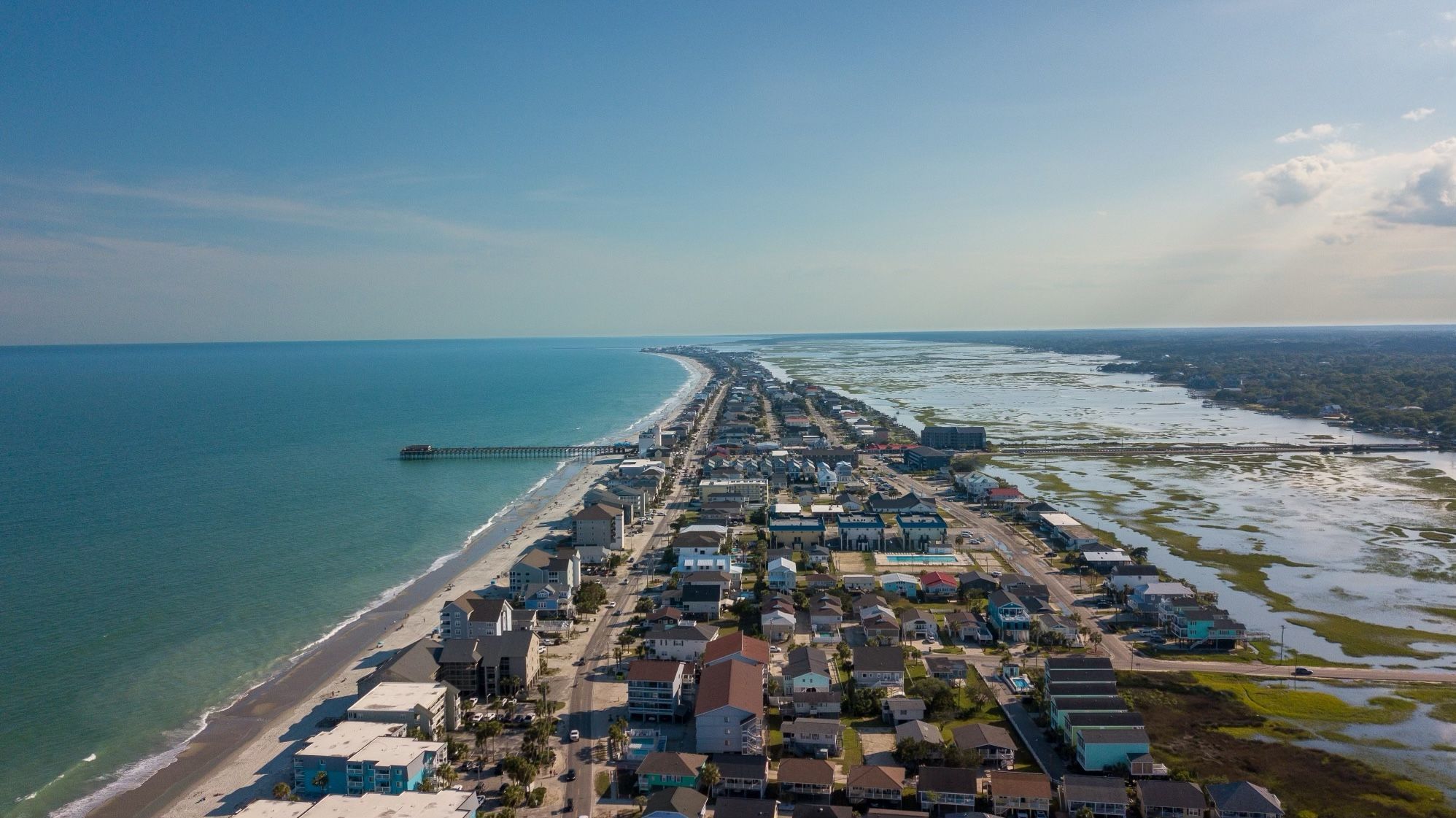 A coastal town with a long beachfront, a pier extending into the ocean, and a mix of residential and commercial buildings.