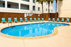 A swimming pool with lounge chairs and a wooden fence.