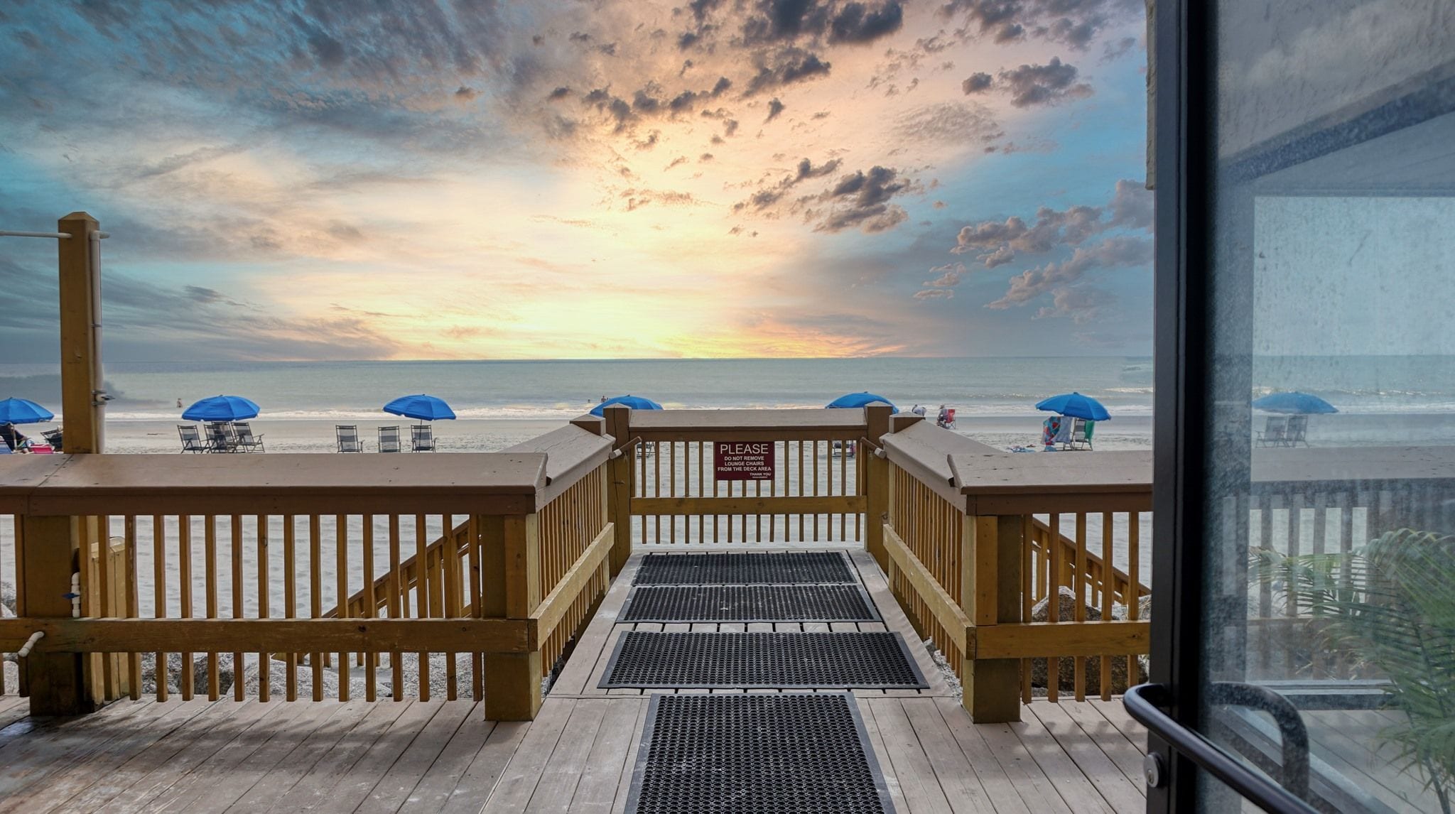 A wooden deck with a view of the beach and ocean.