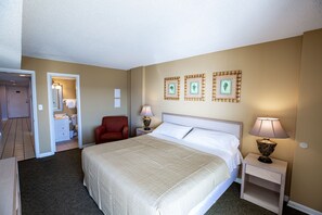 A hotel room with a bed, two bedside tables, a chair, a bathroom, and a door.