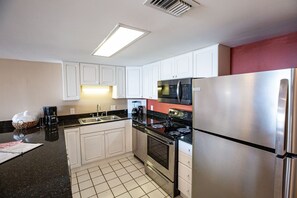 Une cuisine de taille réduite avec des meubles blancs, un réfrigérateur en acier inoxydable, un four à micro-ondes et une cuisinière.
