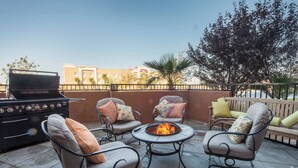 An outdoor patio with a grill, two chairs, a round table, and a fire pit. - Springhill Suites by Marriott Ridgecrest (Ridgecrest)