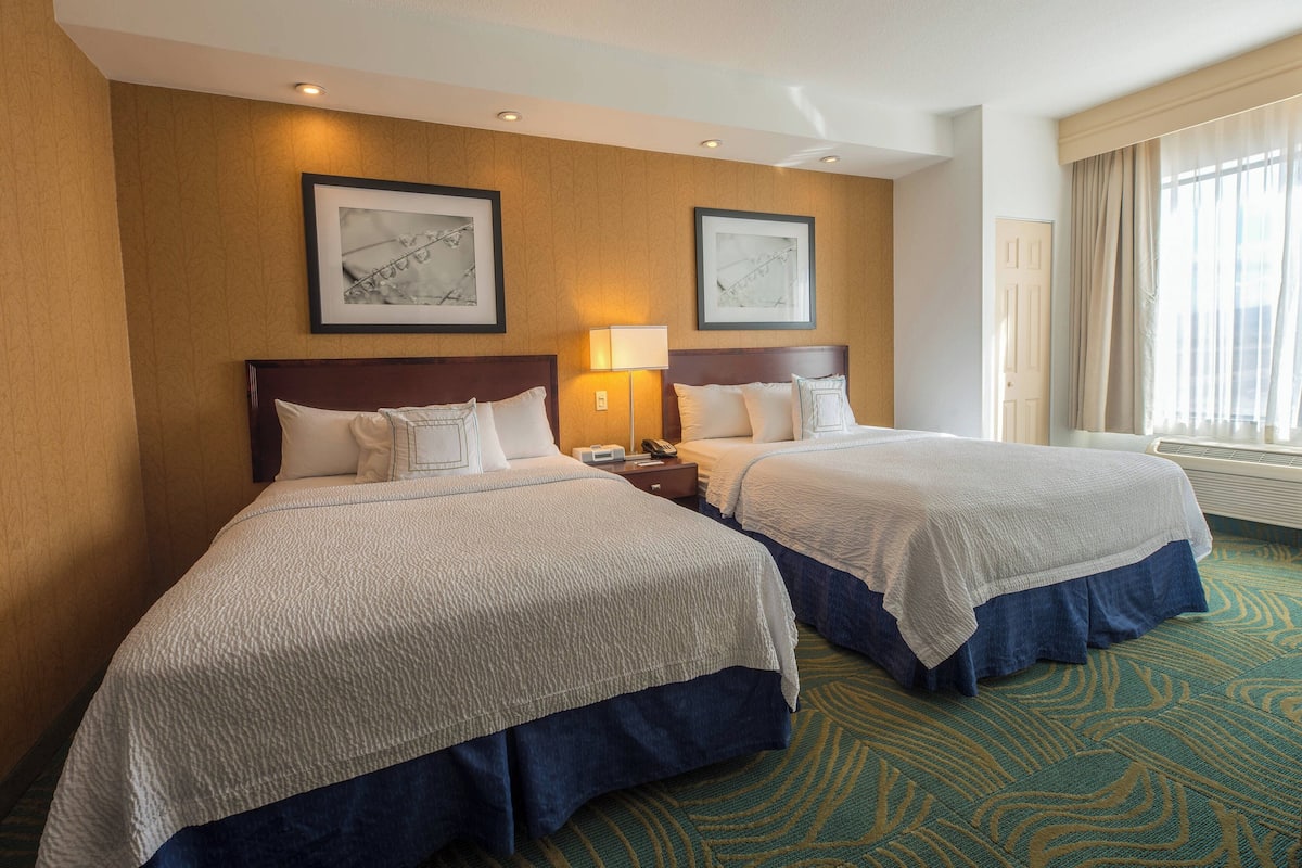 A hotel room with two beds, a large window with curtains, and framed artwork on the wall.