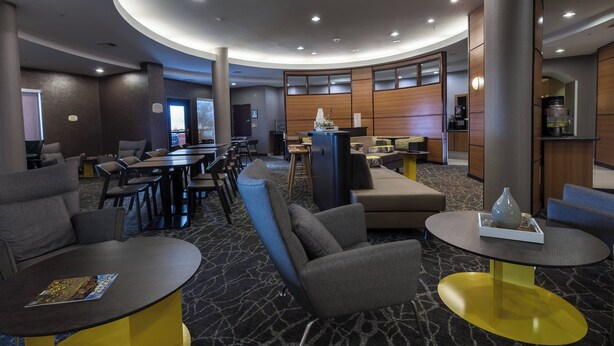 A modern hotel lobby with round tables, comfortable seating, and a central decorative column. - Springhill Suites by Marriott Ridgecrest (Ridgecrest)