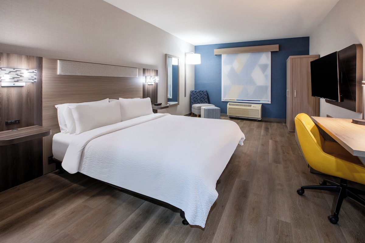 A hotel room with a large bed, a desk, a chair, a television, and a window with blinds.