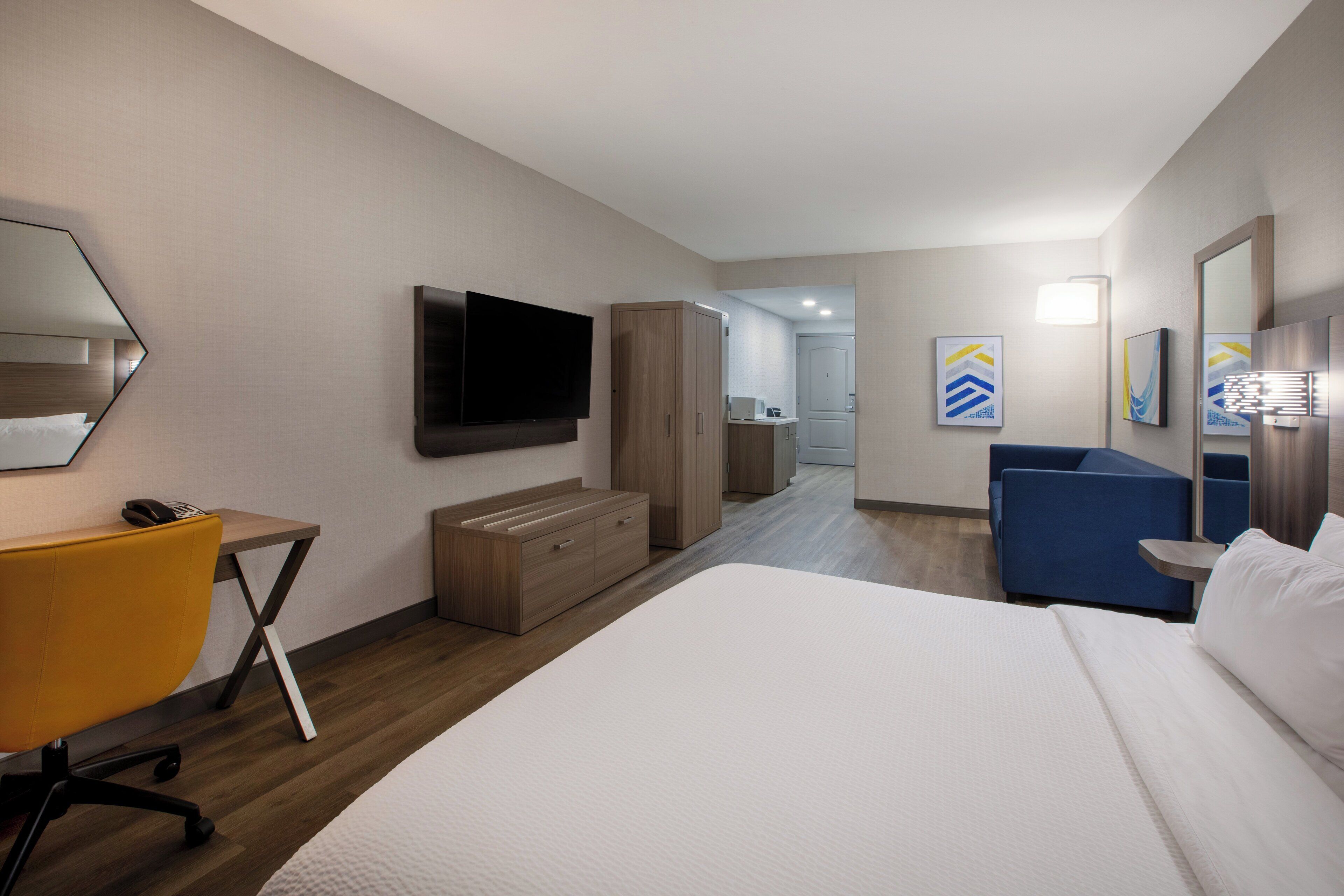 A hotel room with a large bed, a desk with a chair, a TV mounted on the wall, and a blue sofa.
