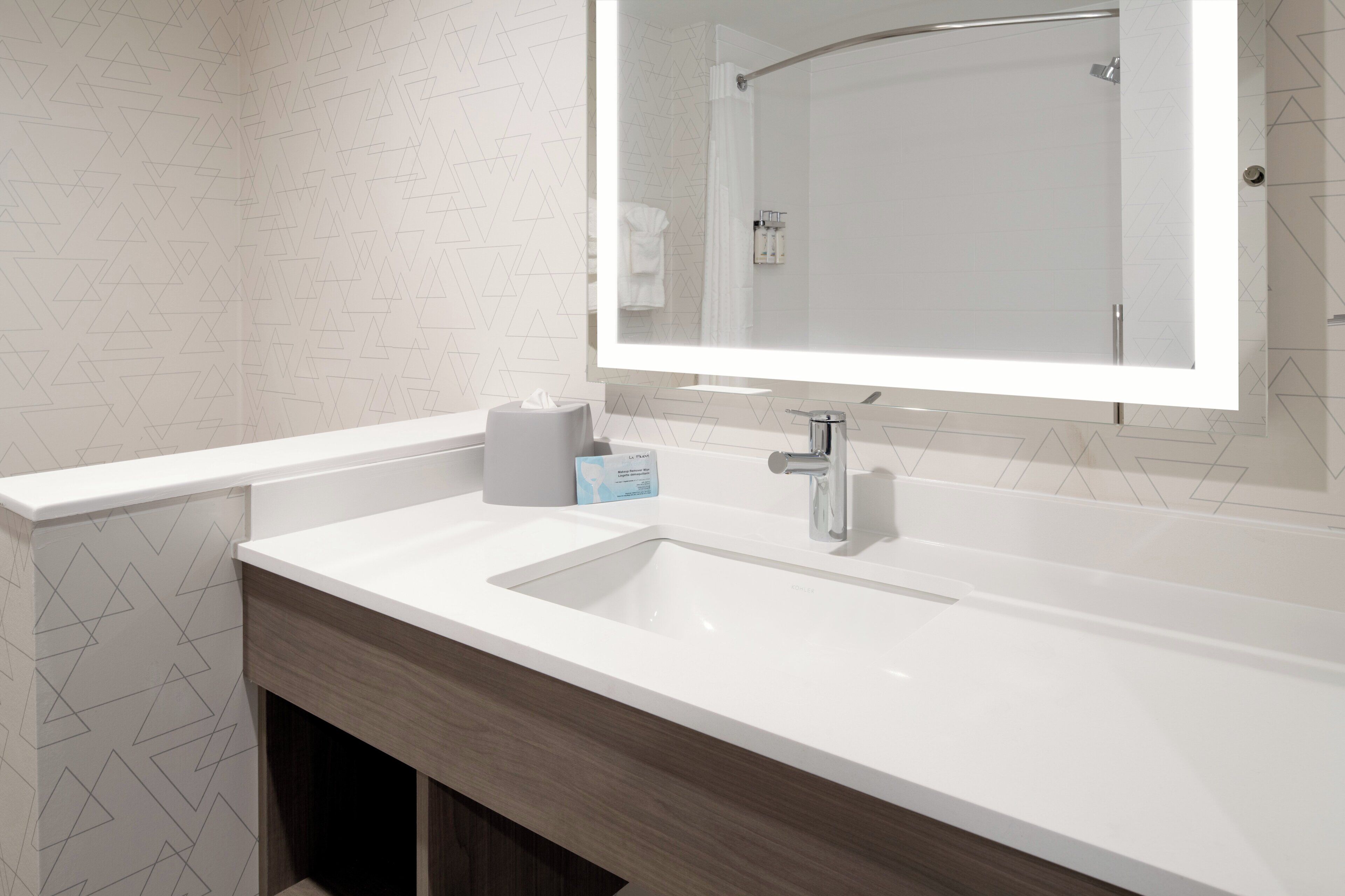 Une salle de bain moderne avec un lavabo blanc, un miroir et un distributeur de serviettes.