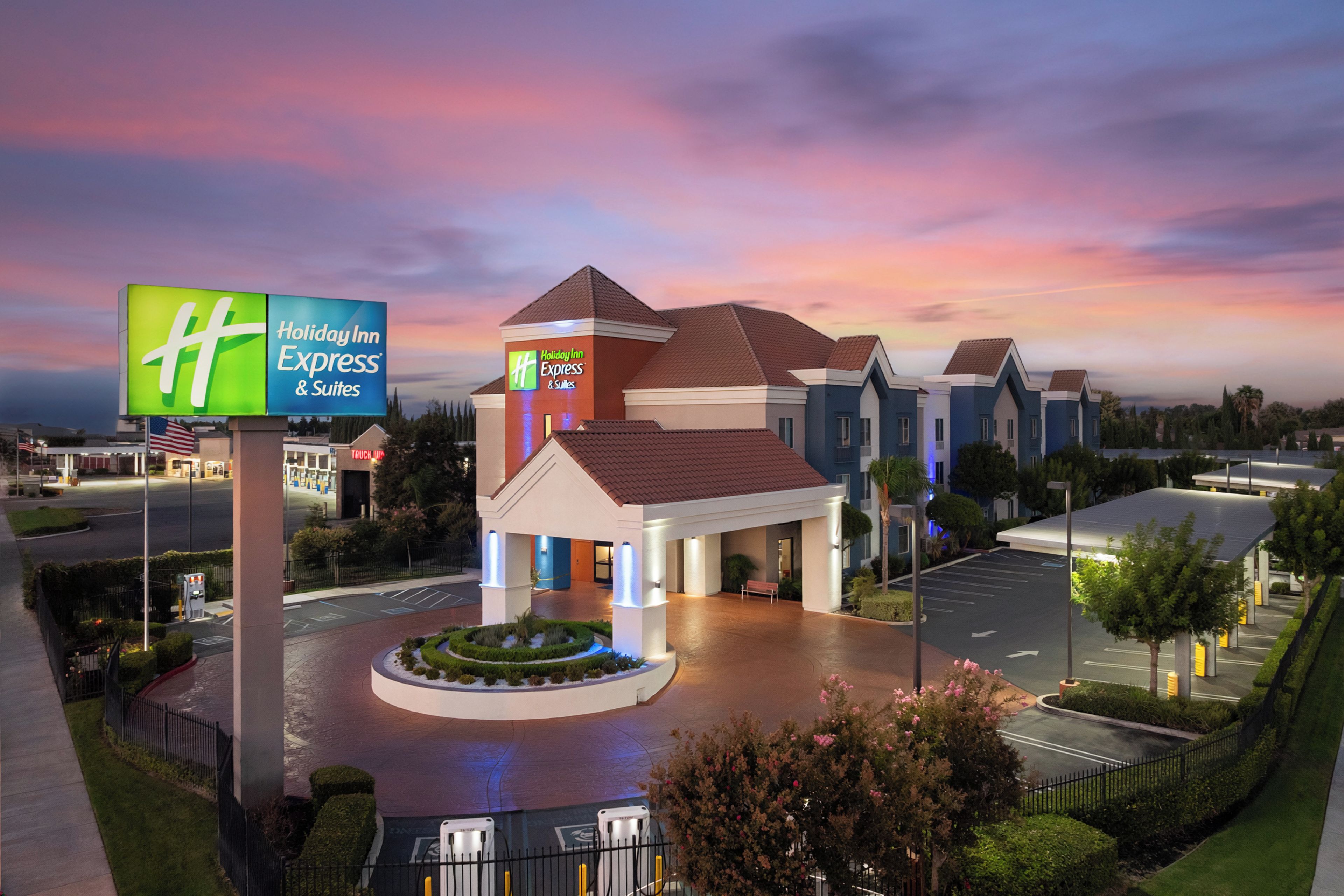 A Holiday Inn Express & Suites with a central entrance, a parking lot, and a landscaped area with a fountain.