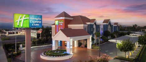 A Holiday Inn Express & Suites with a central entrance, a parking lot, and a landscaped area with a fountain.