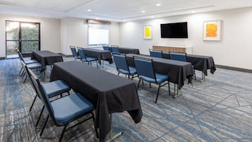 Une salle de conférence équipée de tables et de chaises, dotée d’une grande fenêtre et d’un téléviseur à écran plat fixé au mur.
