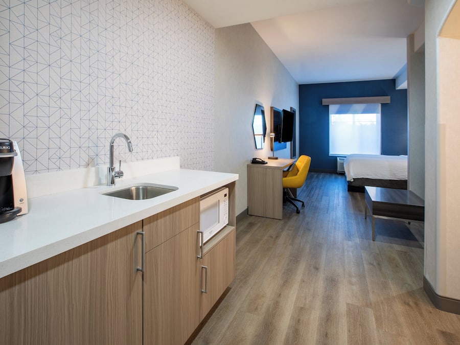 A modern hotel room with a kitchenette, a bed, a desk, and a bathroom.