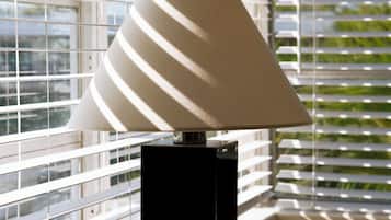 A modern lamp with a conical shade on a black base, positioned in front of a window with horizontal blinds.