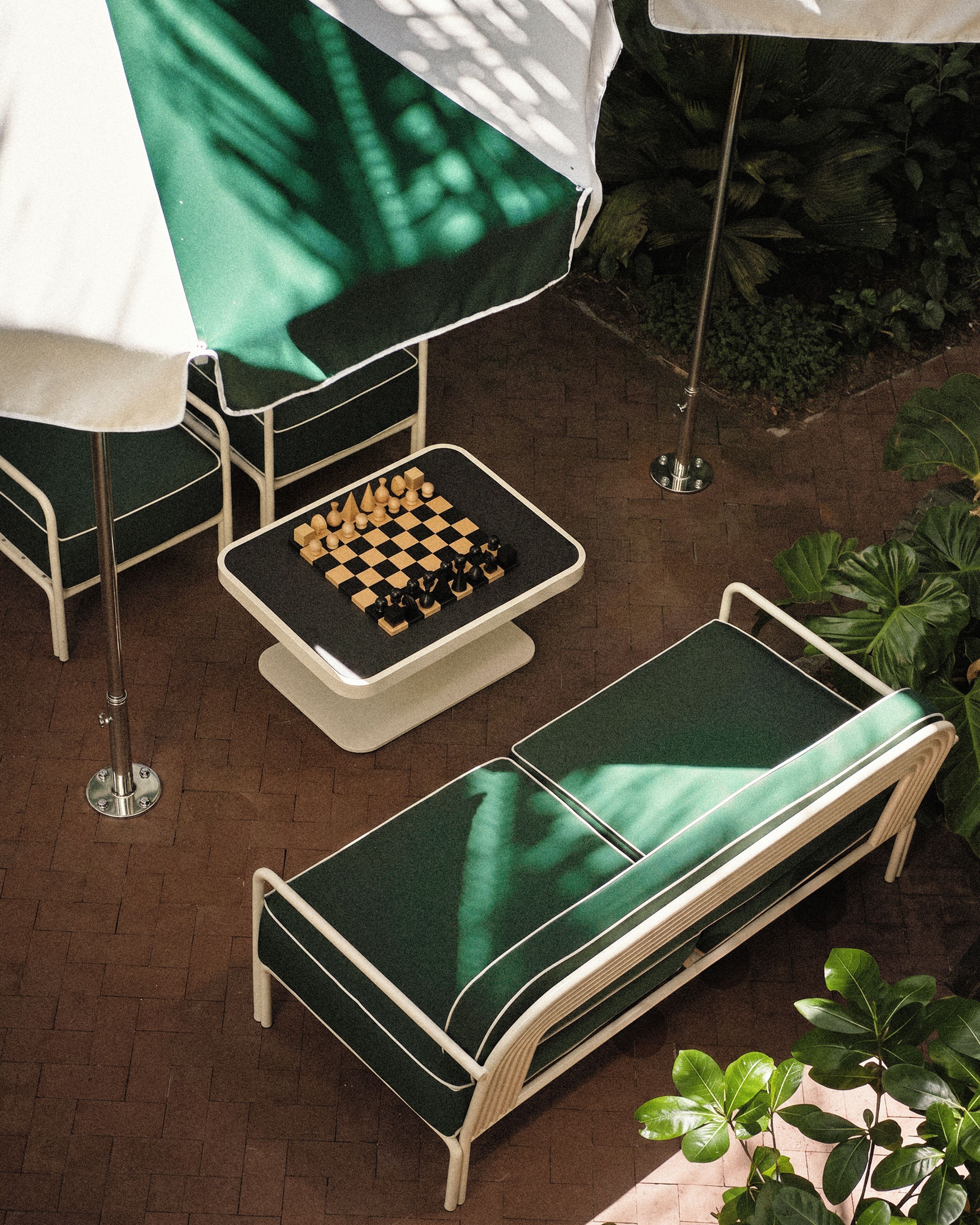 A chessboard on a table, a green lounge chair, and an umbrella.