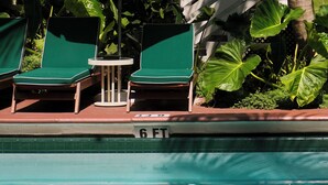 A poolside area with lounge chairs and umbrellas, a palm tree, and a building with a white facade in the background.