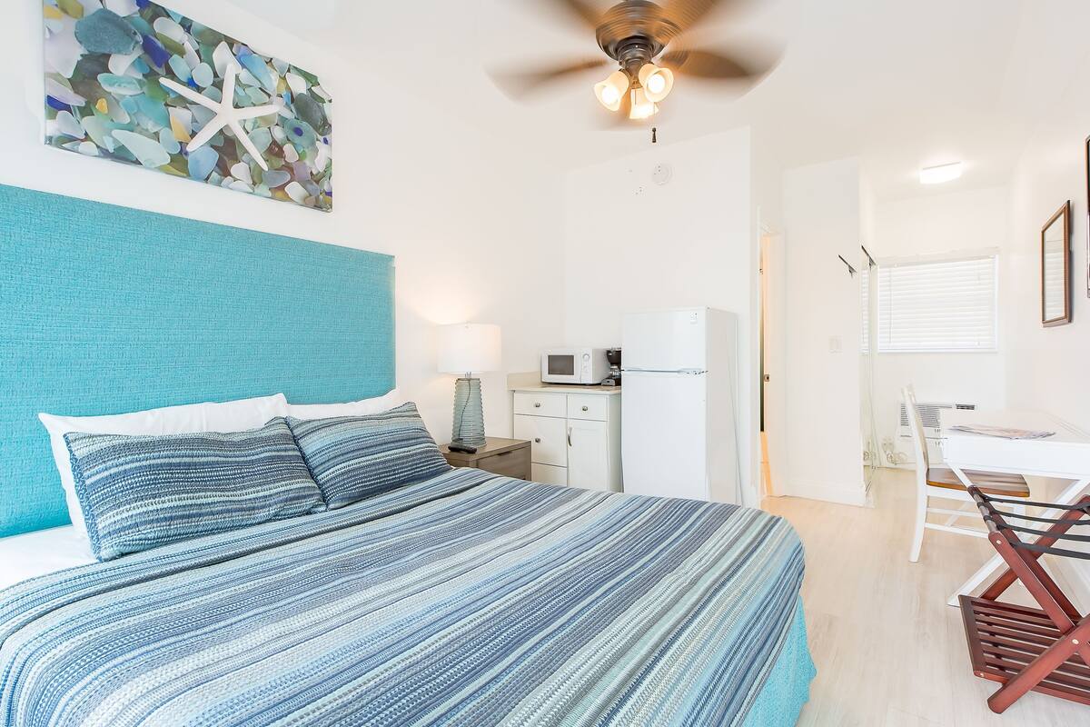 Un dormitorio con cama, ventilador de techo, microondas y una pequeña cocina americana.