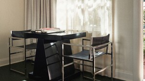 A room with a table and two chairs, a window with sheer curtains, and a view of greenery outside.