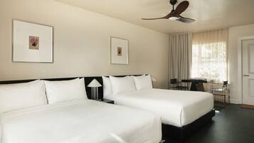 A hotel room with two beds, a desk, a chair, a ceiling fan, and two framed pictures on the wall.