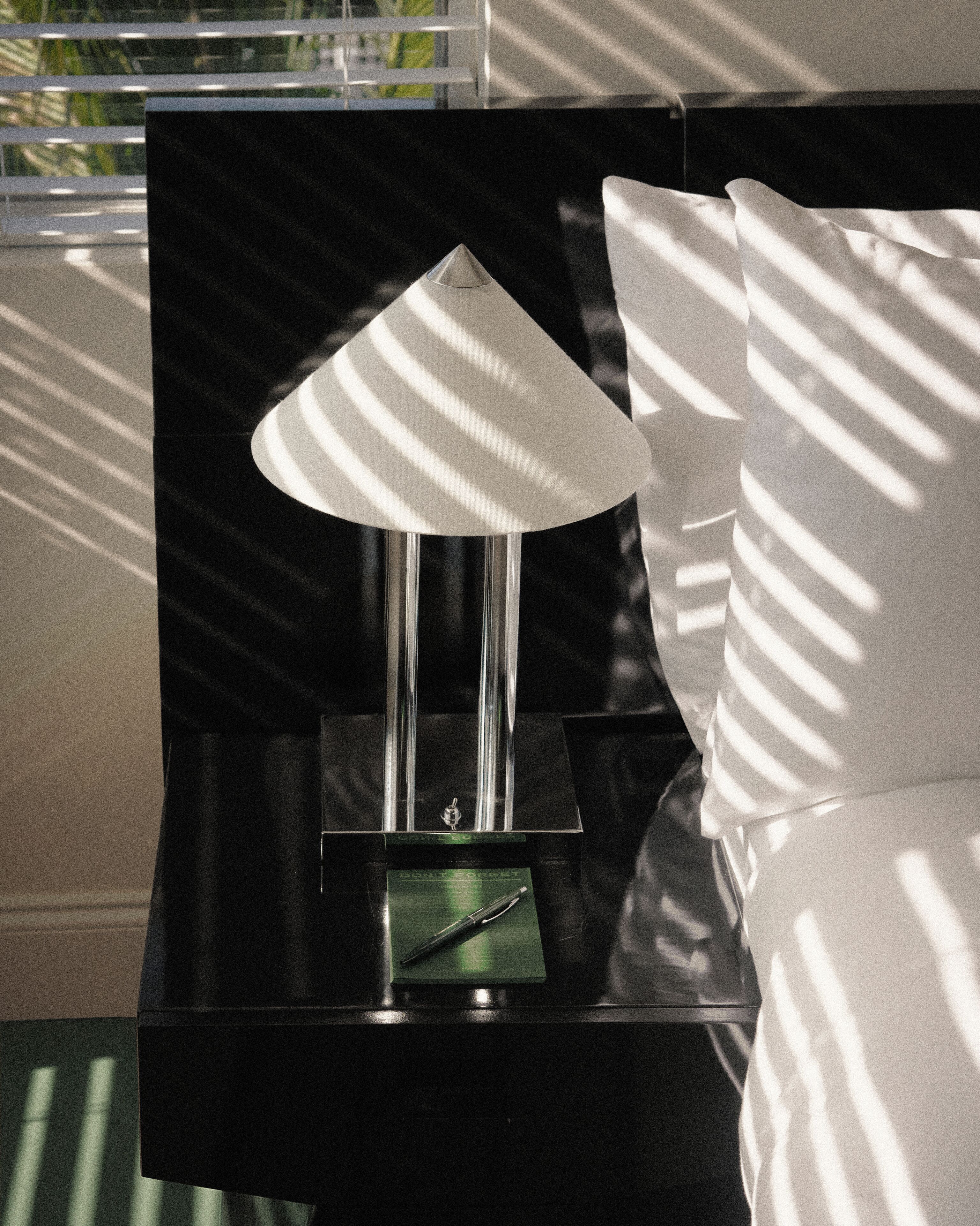 A black bedside table with a clear glass lamp, a green plaque, and a white pillow.
