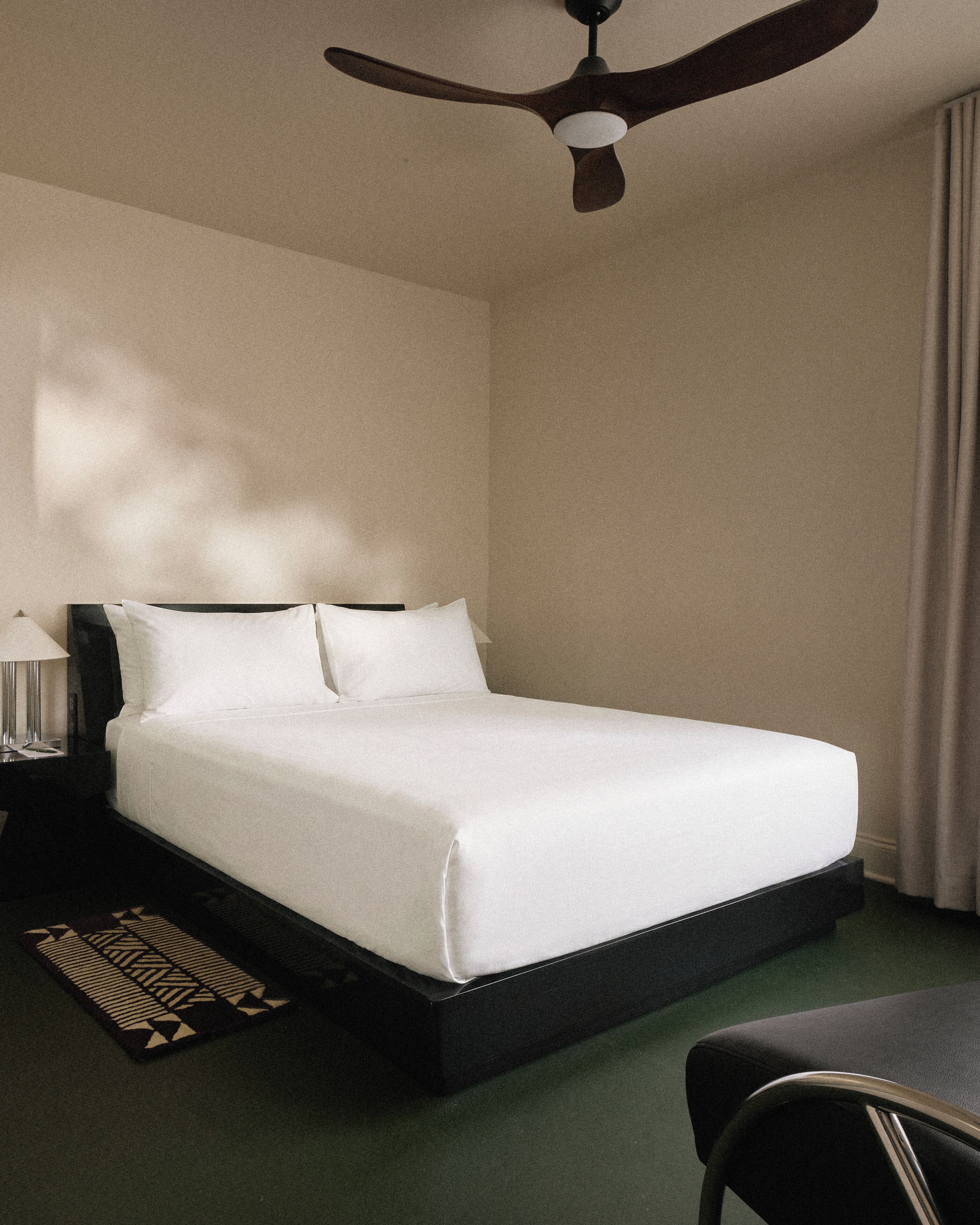 A hotel room with a bed, a nightstand, a lamp, a ceiling fan, and a chair.