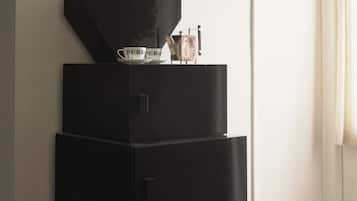 A black refrigerator with a coffee maker and a cup on top, a chair, and a window with curtains.