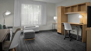 Une chambre d’hôtel équipée d’un bureau, de deux chaises, d’une télévision, d’un radiateur et d’une fenêtre avec des rideaux légers.