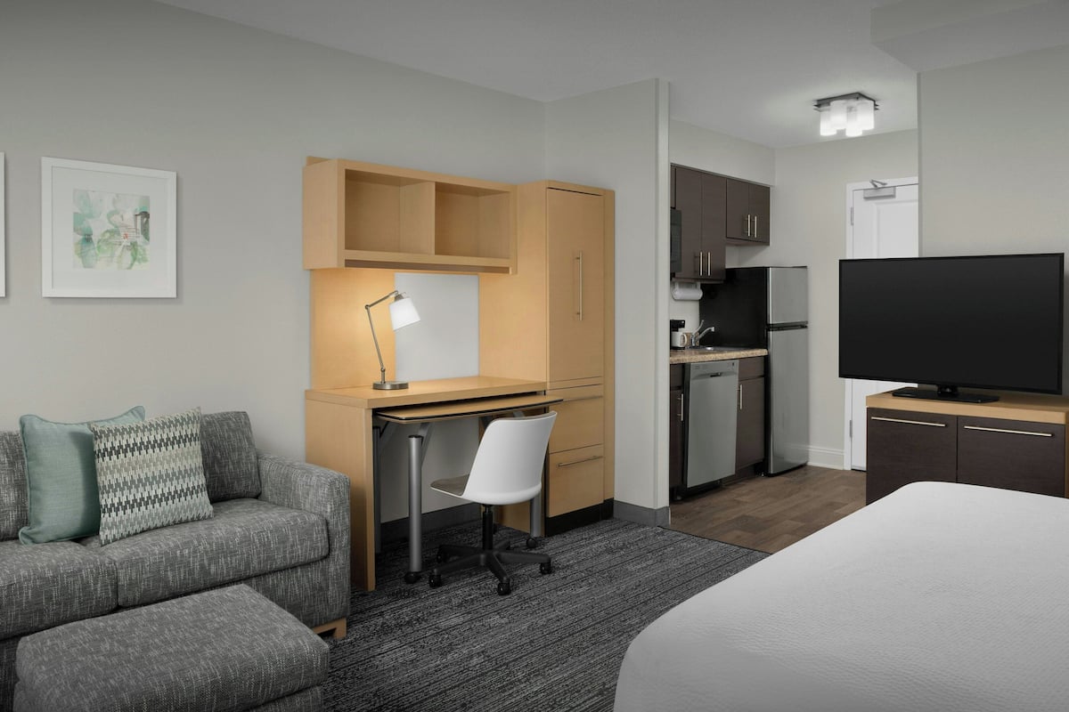 Ein Hotelzimmer mit Bett, Schreibtisch mit Stuhl, einer Küchenzeile und einem Fernseher.