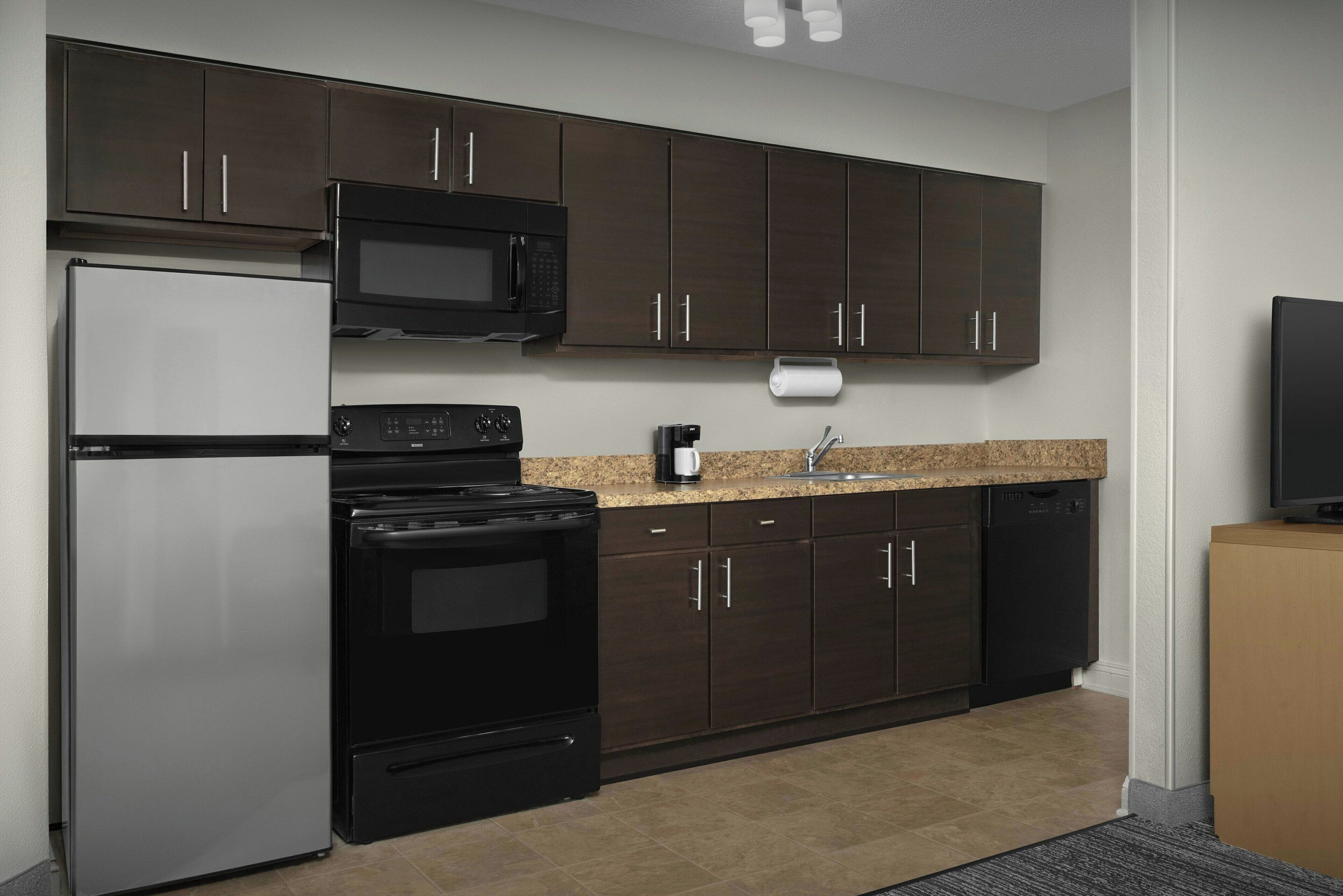 A modern kitchen with dark cabinets, stainless steel appliances, and a granite countertop.