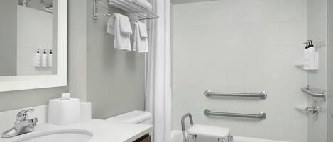 Un baño moderno con lavamanos, inodoro y bañera. Hay toallas y artículos de aseo en la pared.