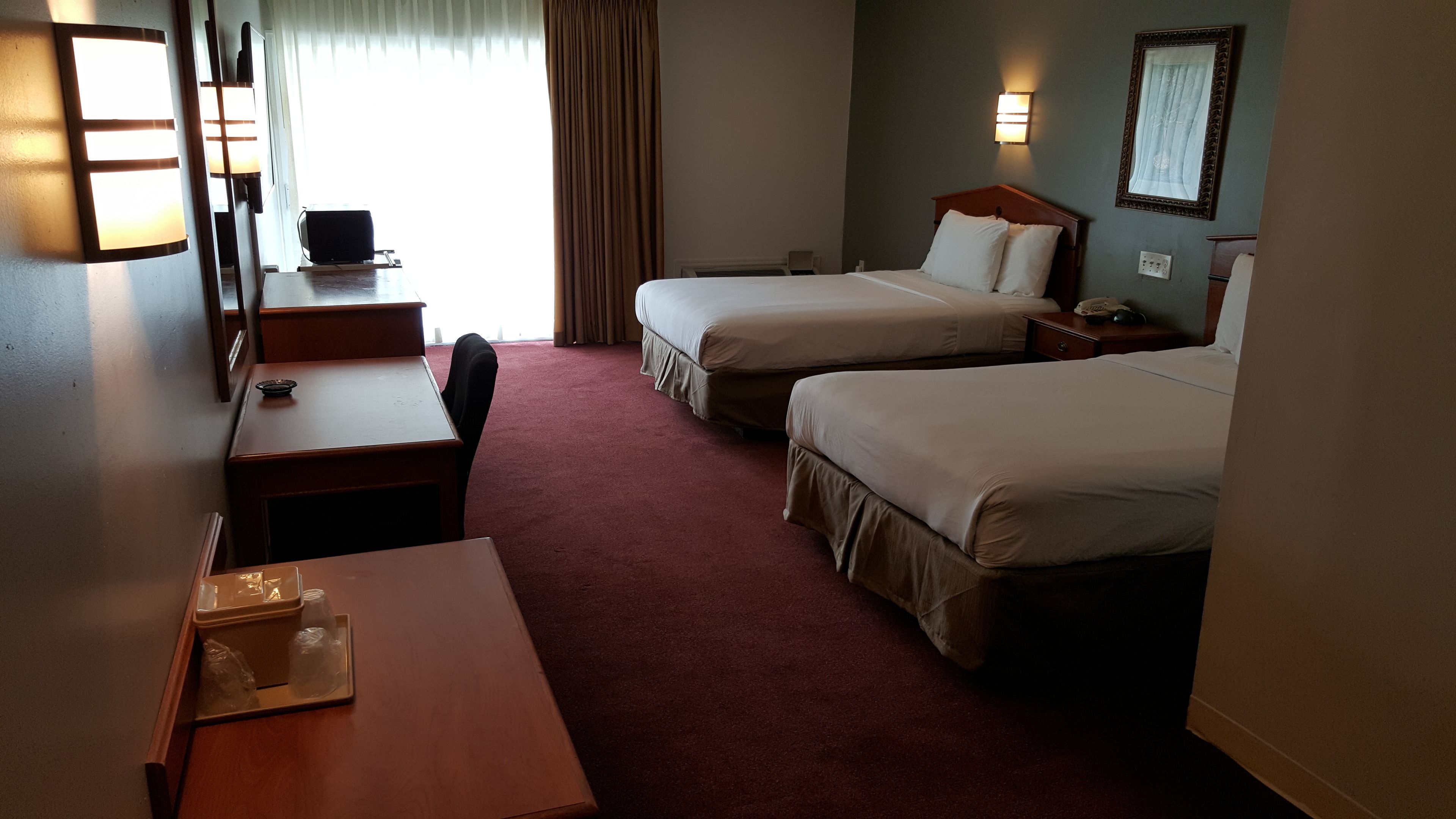 A hotel room with two beds, a desk, a chair, a TV, and a window with curtains.