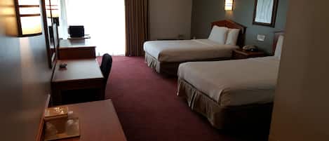 A hotel room with two beds, a desk, a chair, a TV, and a window with curtains.