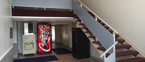A hotel lobby with a staircase, a vending machine, and a refrigerator.