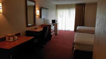 Habitación de hotel con escritorio, silla, cómoda, televisor y dos camas.