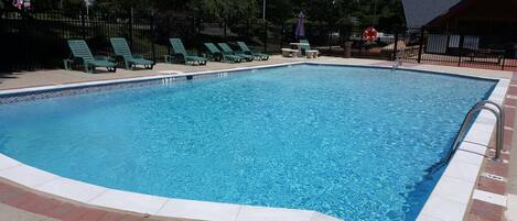 Una piscina rectangular con borde de azulejos, rodeada por un faldón de ladrillo y una cerca de metal.