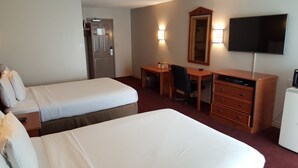 Habitación de hotel con dos camas, un escritorio, una silla, un tocador, un televisor y una puerta.
